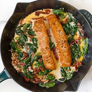 Salmon recipes with a cast-iron skillet full of cooked spinach, a cream sauce and two pieces of salmon