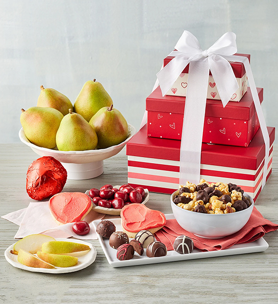 Valentine's Day gifts for her with a stack of red gift boxes tied with a bow surrounded by fruit, chocolate, and cookies.