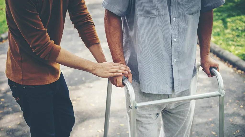 Caregiver helping a person walk with a walker.