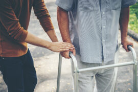 Caregiver helping a person walk with a walker.