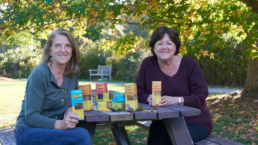 Effie's Homemade Oatcake Biscuits founders sitting on a picnic bench with boxes of cookies.