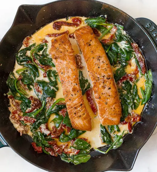 St. Patrick's Day food with two pieces of salmon in a cast-iron skillet with spinach and cream.