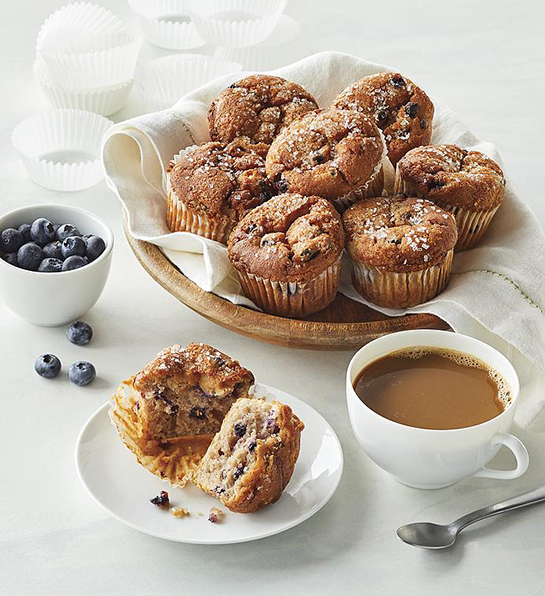 What is gluten with a basket of gluten free muffins next to a cup of coffee and a bowl of blueberries.