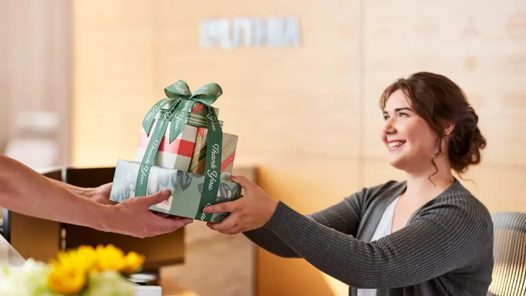 Unique thank you gifts with someone handing a woman sitting behind a desk a stack of wrapped boxes.