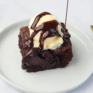 Cherry recipes with a cherry brownie on a plate topped with a scoop of ice cream and chocolate syrup.