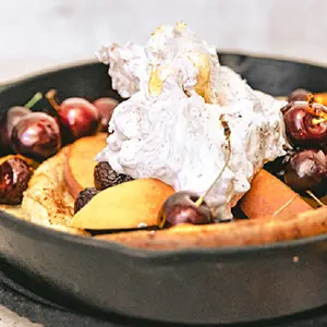 Cherry recipes with a Dutch baby pancake in a cast-iron pan topped with whipped cream and cherries.