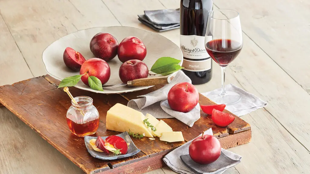 Fruit and cheese pairings with a platter of plums and cheese next to a bottle of wine.