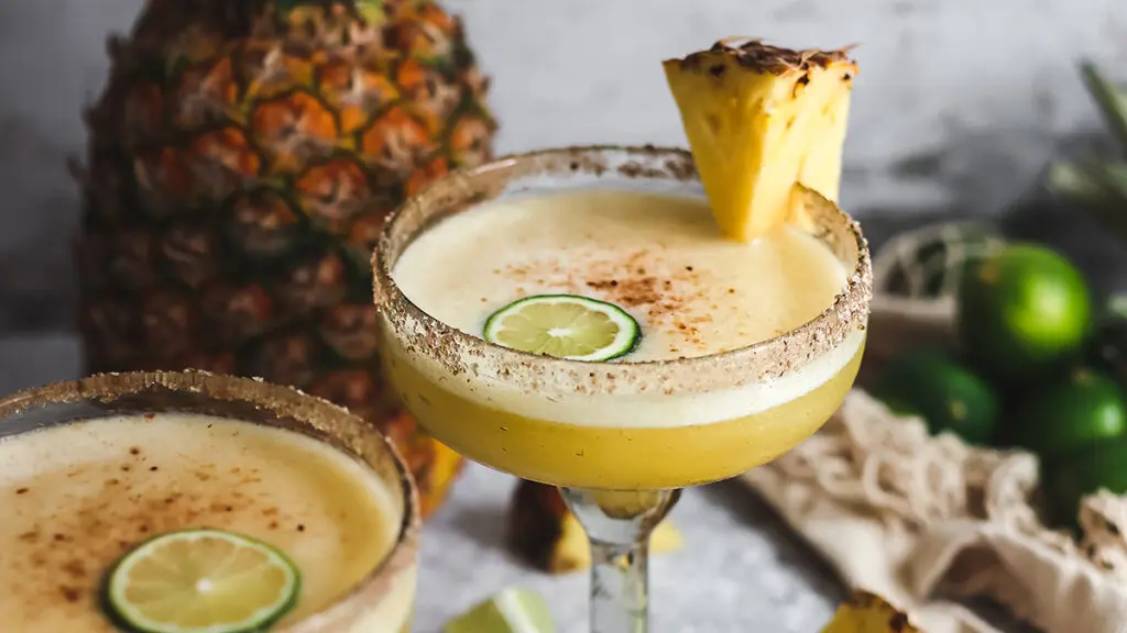 Pineapple margaritas in large glasses with slices of pineapple and lime.