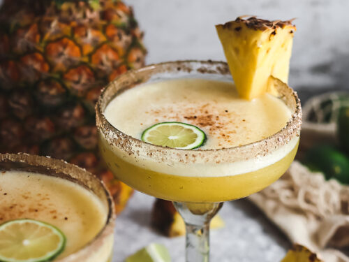 Pineapple margaritas in large glasses with slices of pineapple and lime.