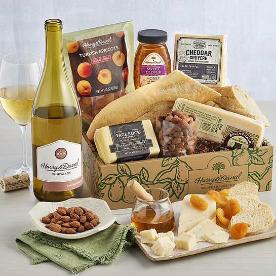 Bottle of chardonnay next to a box of cheese, crackers, nuts and other snacks.