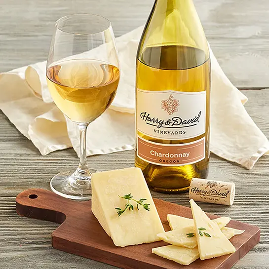 Bottle of chardonnay next to a glass of wine and a cutting board with slices of cheese.