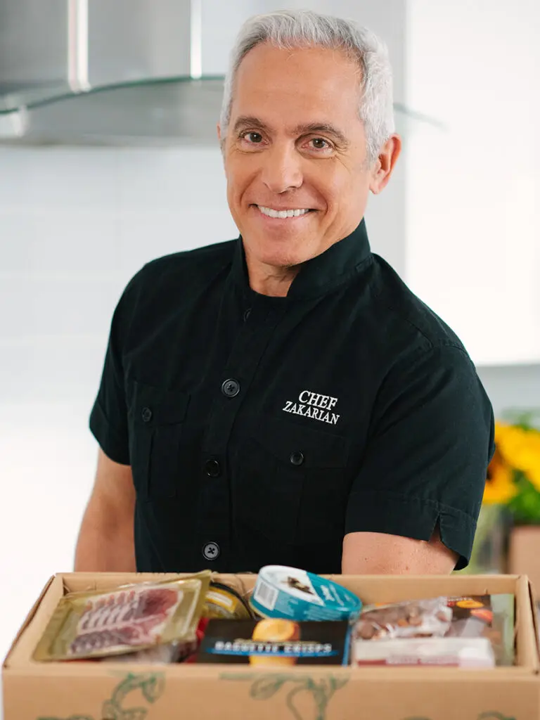 Geoffrey Zakarian holding a box full of pantry items.