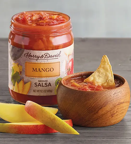 Medium mango salsa in a jar next to a bowl of salsa and slices of mango.