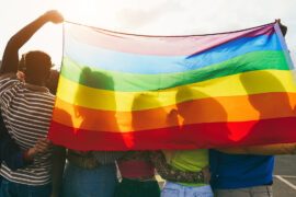 Young diverse people having fun holding lgbt rainbow flag outdoor Main focus on african guy back