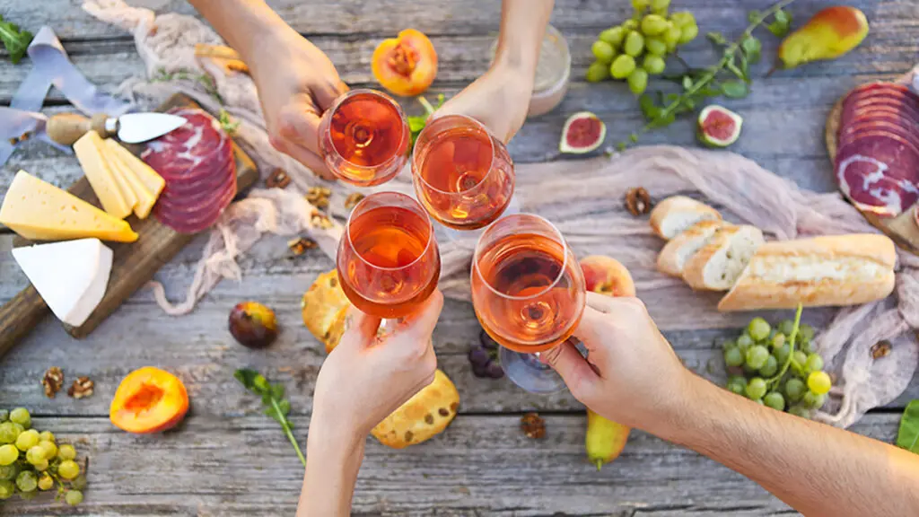 Places to bring rosé with hands clinking glasses over a table spread with food.
