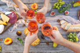 Places to bring rosé with hands clinking glasses over a table spread with food.