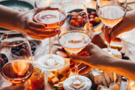 Rosé wine in glasses with hands raising them to clink above a charcuterie spread.