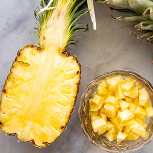 Half a pineapple next to a bowl of pineapple chunks.