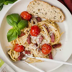 Tomatoes and salami in a pasta dish with a slice of bread.