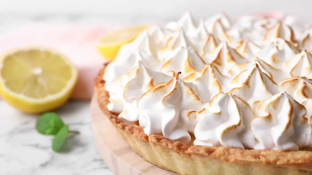 Serving board with delicious lemon meringue pie on white marble