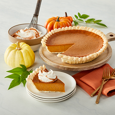 Types of pies with a pumpkin pie next to a mini pumpkin and a bowl of cream.