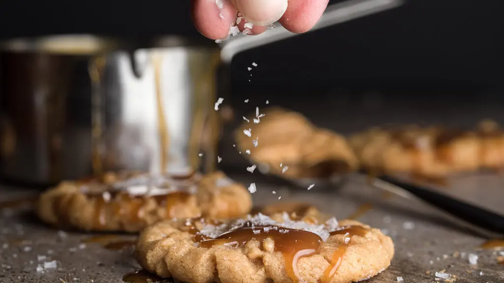 Flavor pairings with a hand sprinkling salt over a caramel cookie.