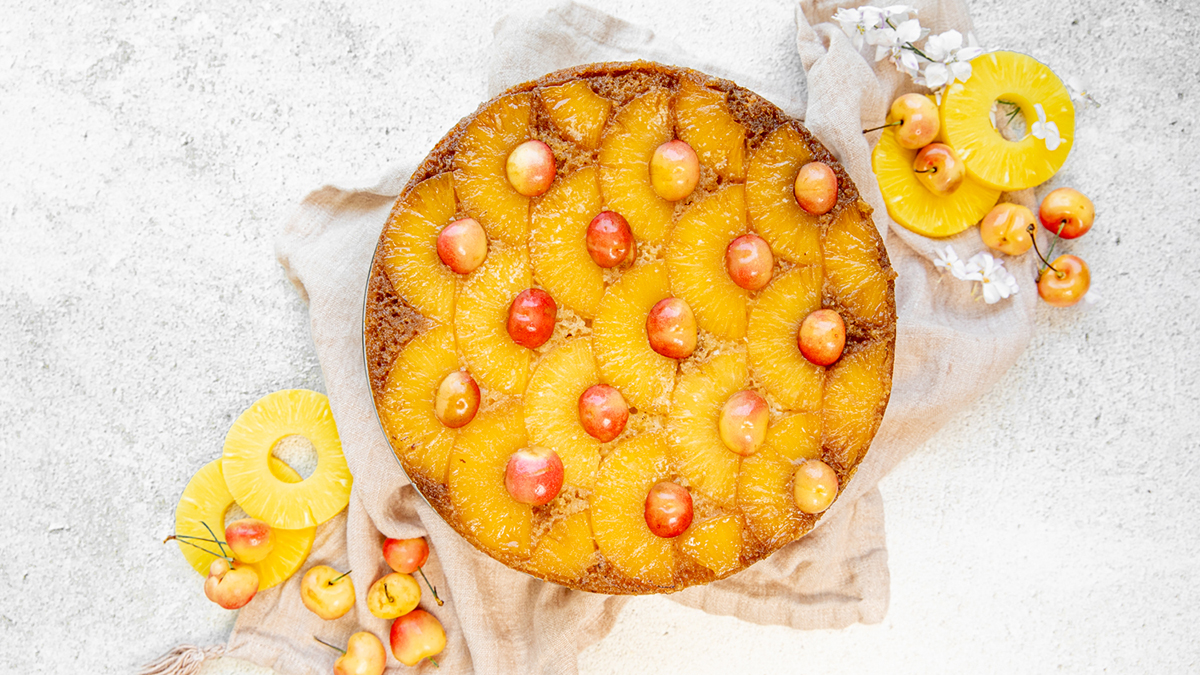 Pineapple upside down cake on a platter surrounded by cherries and sliced pineapple.