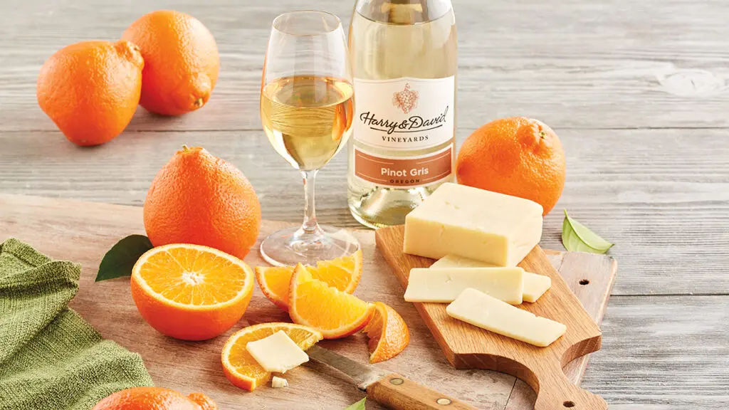 Oranges and cheese next to a glass and bottle of pinot gris.