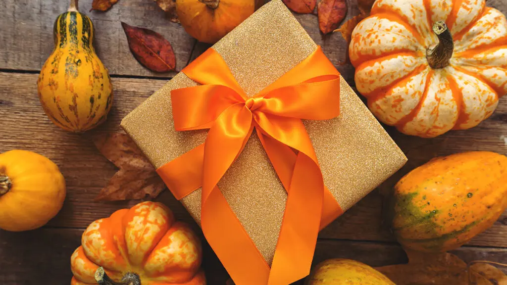 Fall gift wrapped with orange ribbon and surrounded by small pumpkins.