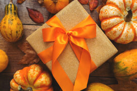 Fall gift wrapped with orange ribbon and surrounded by small pumpkins.