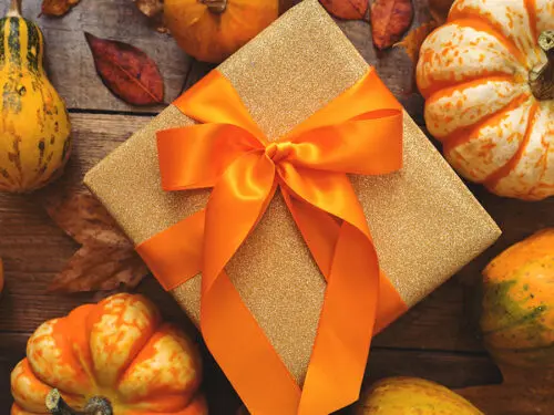 Fall gift wrapped with orange ribbon and surrounded by small pumpkins.