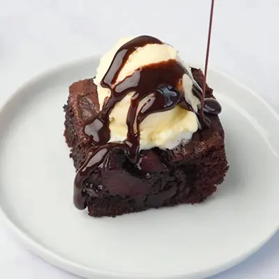 Game day recipes with a cherry brownie topped with ice cream and chocolate sauce on a plate.
