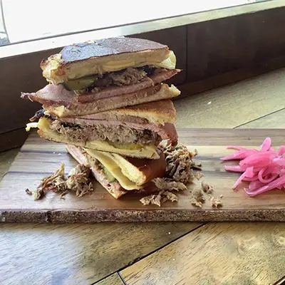 Game day recipes with a stack of Cubano sandwiches on a wooden board.