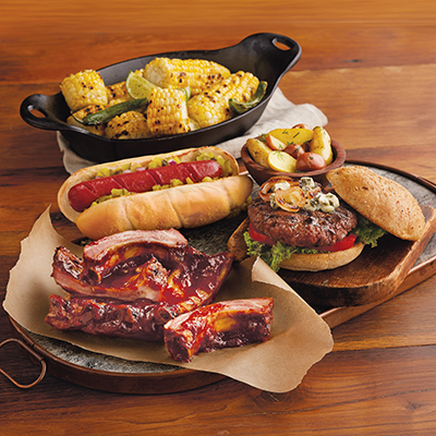 Game day recipes with ribs, burgers, hot dogs, and other dishes on a wooden table.
