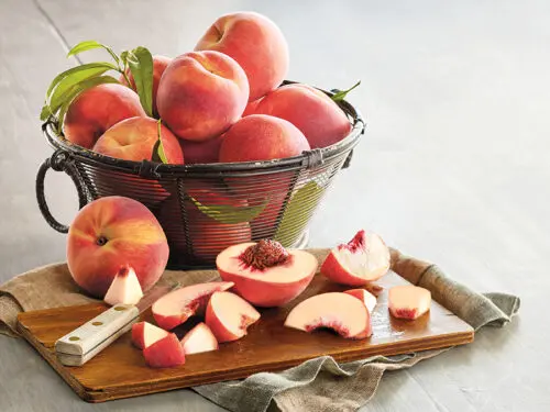 Peppermint peaches in a basket with slices of peaches on a board in front.