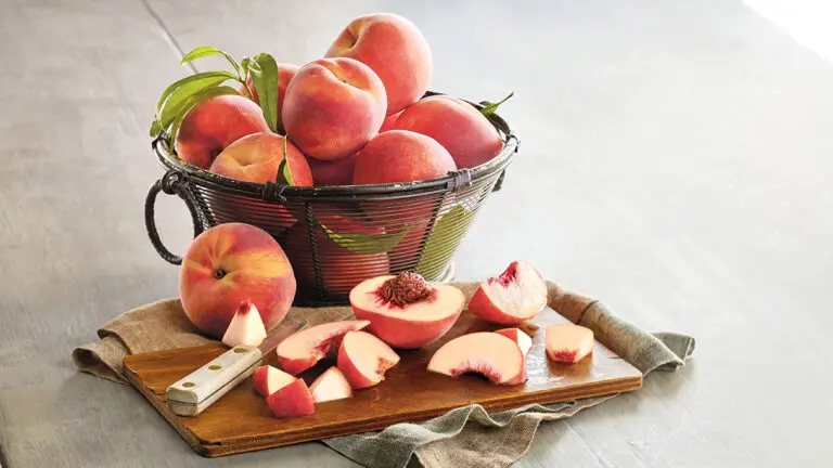 Peppermint peaches in a basket with slices of peaches on a board in front.