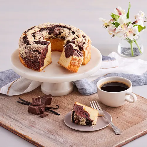 Types of cake with a platter of coffee cake next to a cup of coffee and a slice of cake.