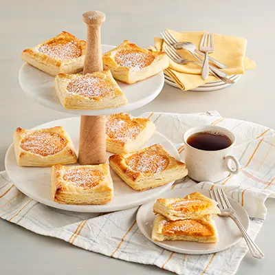 Types of pastries with trays of danishes next to a cup of coffee.