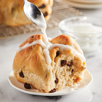 Types of pastries with a hot cross bun being iced.