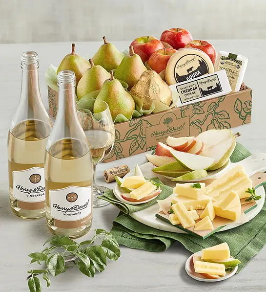 Cheese gifts with a box of pears, apples, and cheese next to two bottles of white wine.