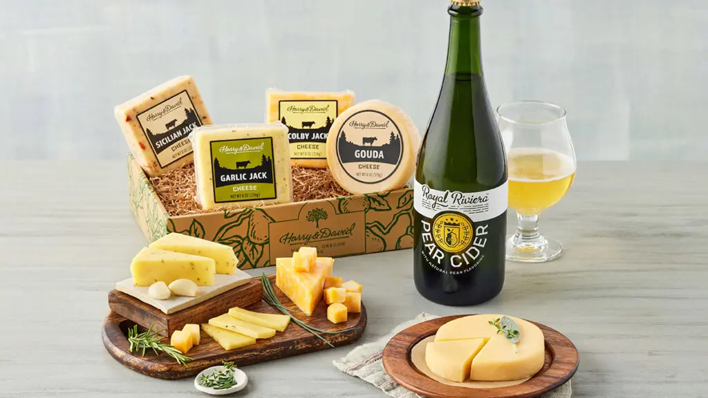 A bottle of pear cider next to a crate of cheese.