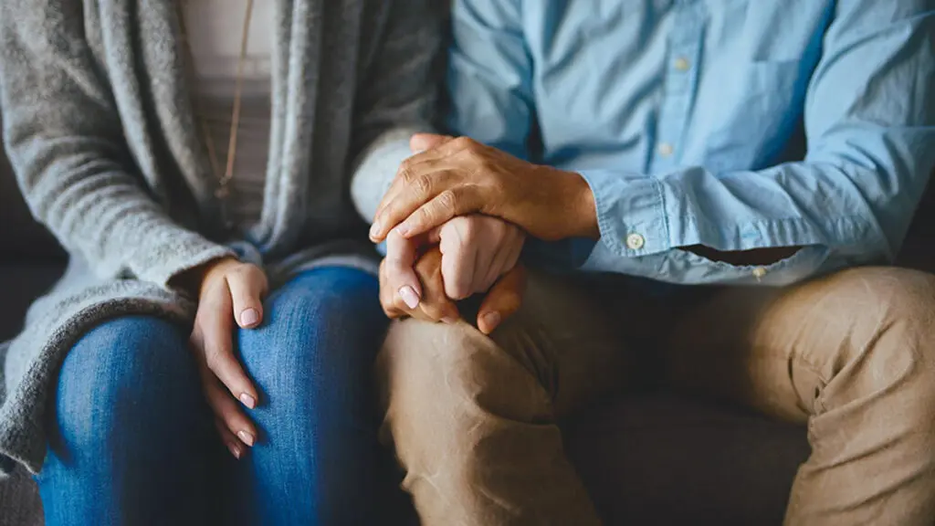 Two people holding hands and sitting shiva.