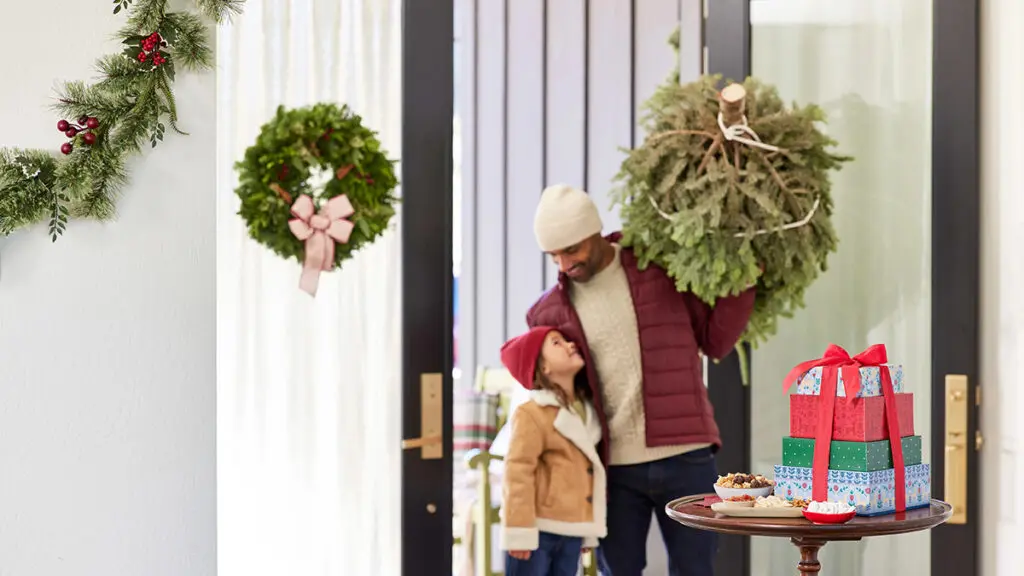 Christmas scents with man and young girl walking into a house with a Christmas tree.