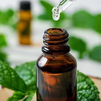 Peppermint oil with peppermint leaves in the background.