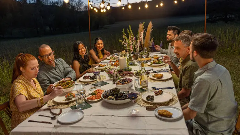 How are holidays created with a group of people sitting outside at a table covered with food.