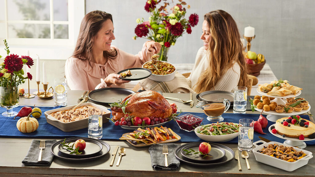 How holidays are created with two women sitting at a Thanksgiving table and serving food.