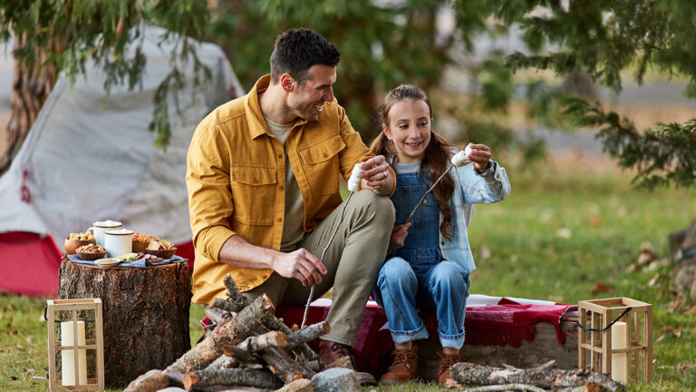 Father and daughter making s'mores at a campfire.