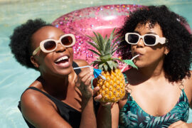 Two Black friends drink pineapple drink in the swimming pool on summer vacation