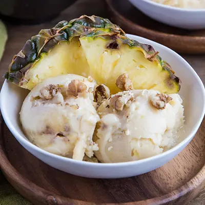 A bowl of pineapple nice cream with pineapple wedges.
